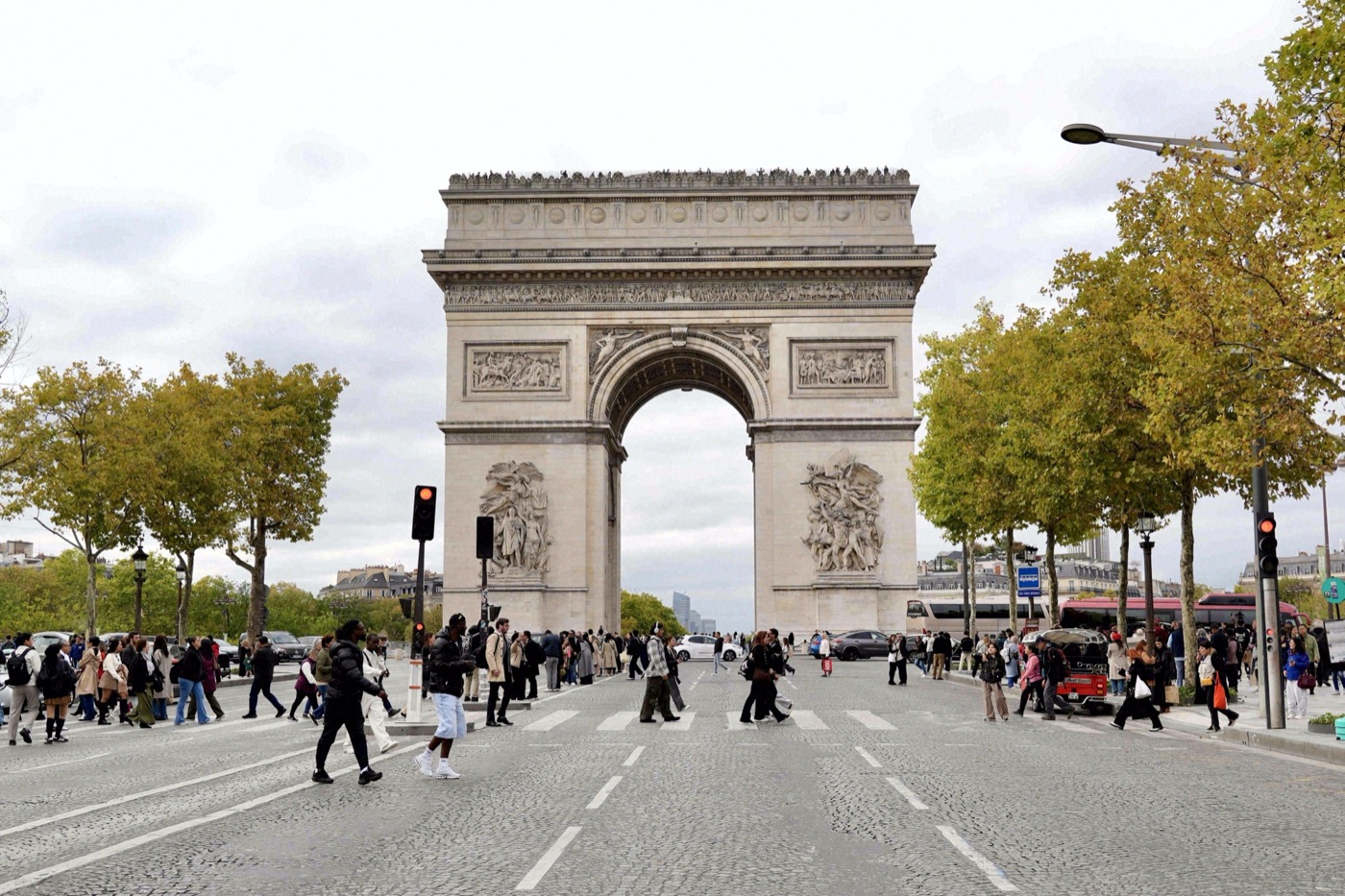 Fußgänger überqueren die Straße vor dem Arc de Triomphe, flankiert von herbstlich gefärbten Bäumen der